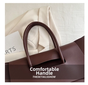 Detail shot of the smooth brown leather handle and texture on a minimalist tote bag