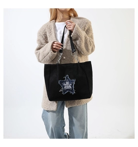 Detail of black suede tote bag featuring a blue frayed denim star patch and chain straps