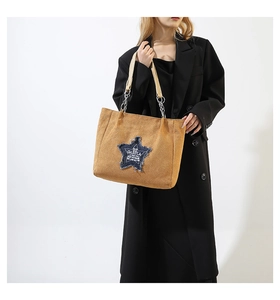 Detail of star denim patch and chain strap on khaki tote bag worn with black blazer