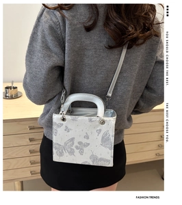 Detail of silver crossbody bag with butterfly prints and metallic handle on model