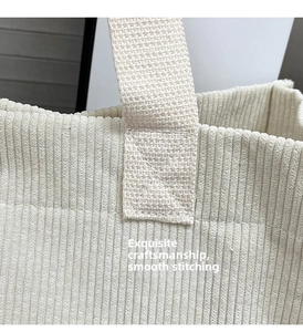 Detail of reinforced cross-stitching on corduroy tote bag handles and beige fabric texture