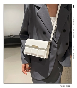 Detail of white waffle texture crossbody bag with gold metal trim on gray suit
