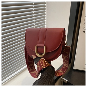 Detail of wine red leather saddle bag with gold U-shaped buckle and jacquard strap