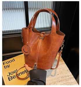 Vue détaillée du sac seau marron avec serrure métallique et breloque smiley sur pierre