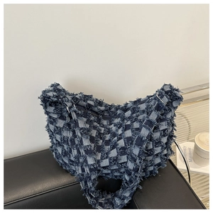 Detail of blue denim fringe tote with distressed plaid pattern and textured frayed edges