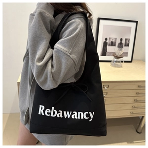 Minimalist black canvas tote bag with Rebawancy print and bow detail shown on a model