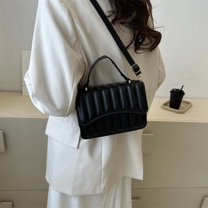 Moderne schwarze Stepp-Umhängetasche mit Goldakzenten an Model in weißem Anzug