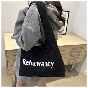 Detail of black canvas tote bag with bow tie decoration and white logo lettering
