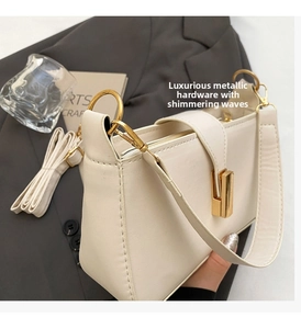Detail of cream baguette bag featuring gold twist lock and adjustable shoulder strap