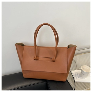 Minimalist brown leather tote bag with unique handle detail on a modern sofa background