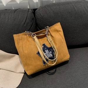 Yellow suede tote bag with denim star patch and metal chain strap on gray sofa