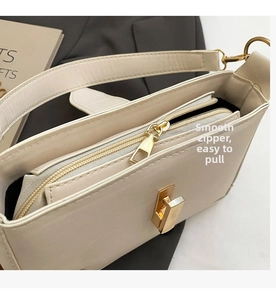 Close-up of cream leather shoulder bag showing gold square buckle and smooth zipper pocket