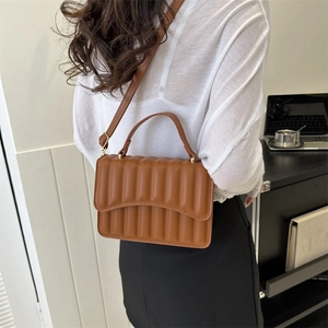 Braune Umhängetasche aus Leder mit Faltendesign in einer minimalistischen Büroumgebung