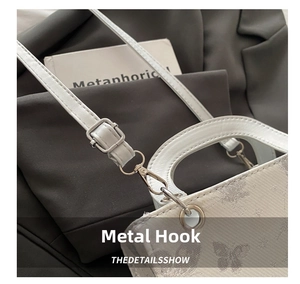 Detail of silver metal hooks and butterfly pattern on white leather crossbody bag