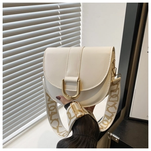 Detail of a creamy white saddle bag with golden U-shaped clasp and wide patterned strap