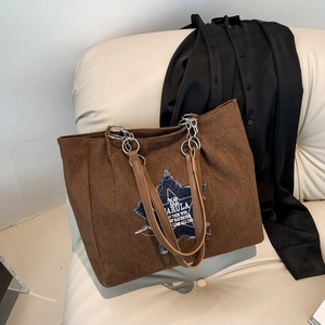 Brown suede tote bag with denim star patchwork and chain shoulder strap on sofa