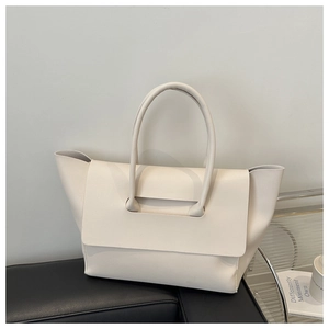 Detail of minimalist cream leather tote bag placed on a modern black leather sofa