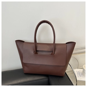 Detail of a deep brown leather tote bag with unique flap closure and cylindrical handles