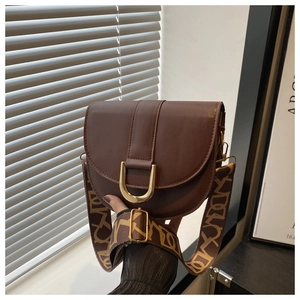Detail of a brown saddle bag featuring a gold horseshoe buckle and retro patterned strap