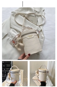 Close-up of white crocodile pattern cylinder bag with silk scarf handle and bear charm
