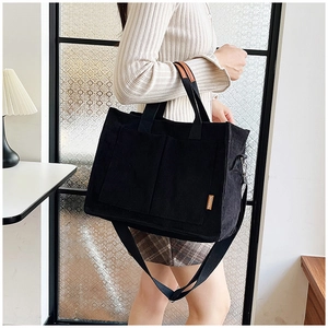 Detail of black corduroy tote bag showing ribbed texture and fashion label on the strap