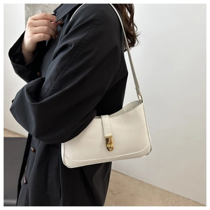 Close-up of a white minimalist half-moon baguette bag with a sleek golden metal clasp