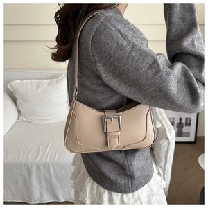Detail of beige leather shoulder bag featuring a large silver metal buckle and stitching