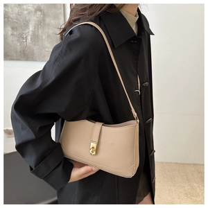 Close-up of minimalist beige leather underarm bag featuring a vintage gold clasp on model