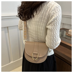 Detail of beige saddle bag featuring gold D-buckle and jacquard wide shoulder strap