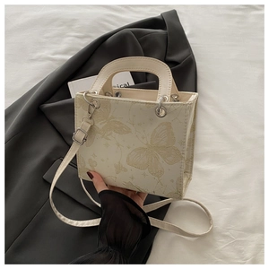 Detailed close-up of cream butterfly print handbag placed on a dark grey suit jacket