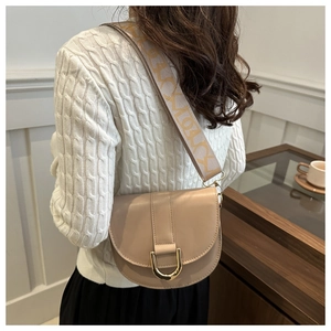 Detail of beige saddle bag with jacquard woven strap and golden horseshoe buckle