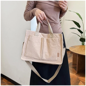 Detail of beige corduroy tote bag with dual front pockets and brown leather brand label