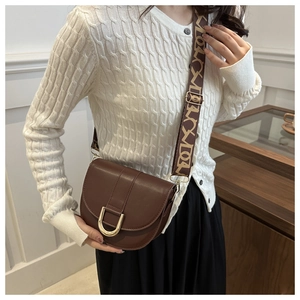 Detail of a brown leather saddle bag with a golden U-shaped buckle and a patterned strap