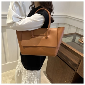 Detail view of a large brown leather tote bag with unique strap and flap design