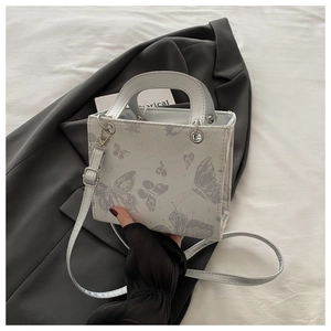 Detail of silver butterfly print and metallic charms on small white structured tote bag