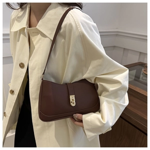 Detail of dark brown leather underarm bag with gold buckle on beige trench coat