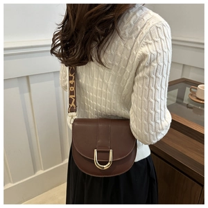 Detail of a dark brown leather saddle bag featuring a gold D-buckle and wide patterned strap
