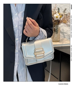 Sac bandoulière argenté structuré avec boucle dorée porté par un mannequin en costume