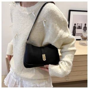 Minimalist black matte leather underarm bag with gold metal clasp on ivory knit outfit