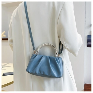 Detail of blue dumpling bag with pearl handle and pleats on a white blazer outfit