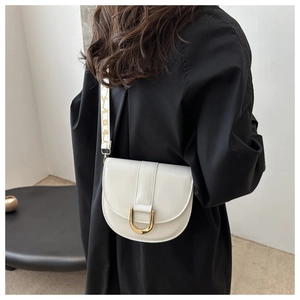 Detail of white saddle bag featuring gold U-buckle and jacquard strap on a model