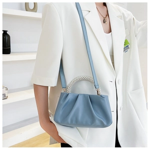 Detail of blue pleated cloud bag with pearl handle and leather strap on white suit