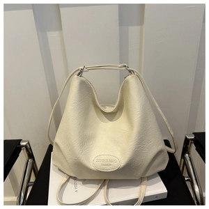 Detail of cream pleated shoulder bag with leather logo patch on minimalist background