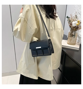 Detail of a black leather flap bag featuring geometric textures and a silver metal bar