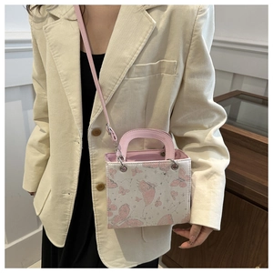 Detail of a white crossbody bag with pink butterfly prints and top handle on a model
