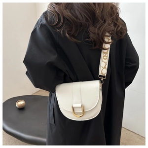 Detail of white semi-circular saddle bag featuring a wide patterned strap and gold horseshoe clasp