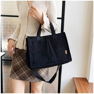 Detail of black corduroy tote bag showing front double pockets and fashion logo label