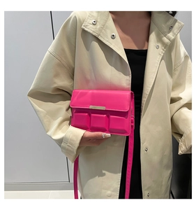 Detail of hot pink crossbody bag with square textures and gold metal bar on beige coat