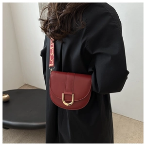 Detail of dark red saddle bag with gold buckle and vintage jacquard strap on model