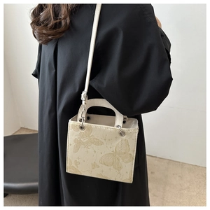 Detail of square crossbody bag featuring embroidered gold butterflies and silver hardware